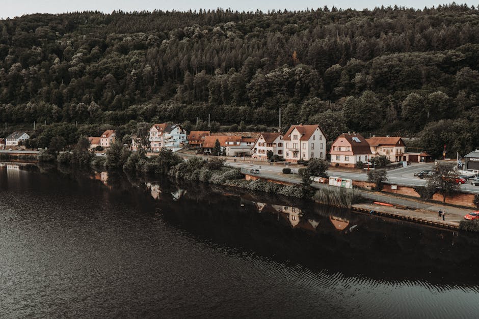 Quiet European town nestled between lush forests and a serene river, reflecting beauty and tranquility.