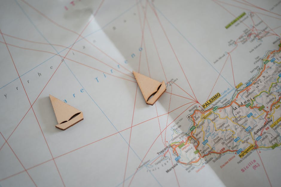 Flat lay of a nautical map with sailboat cutouts representing travel planning to Sicily.